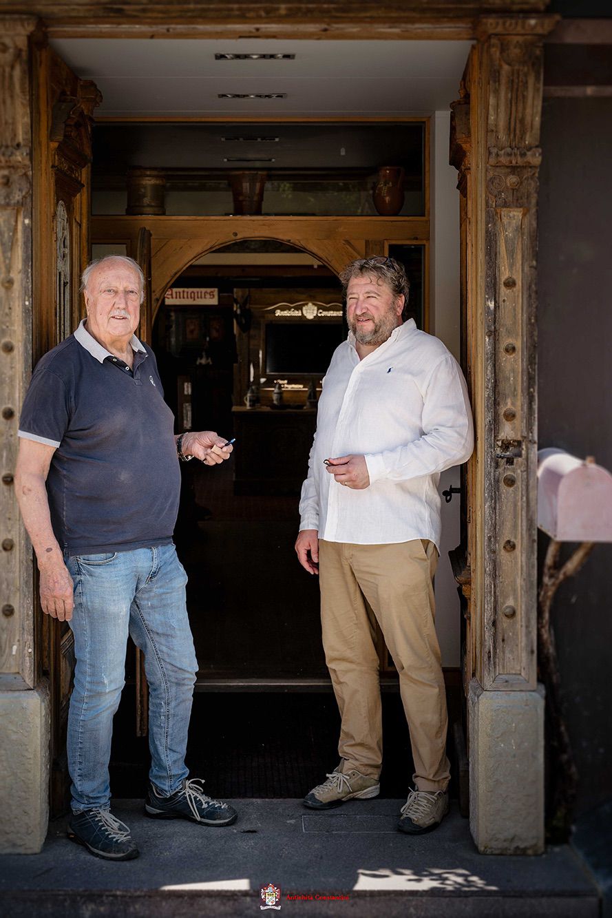 Leopoldo e Luca Constantini sulla soglia, incorniciati da un portale in legno intagliato