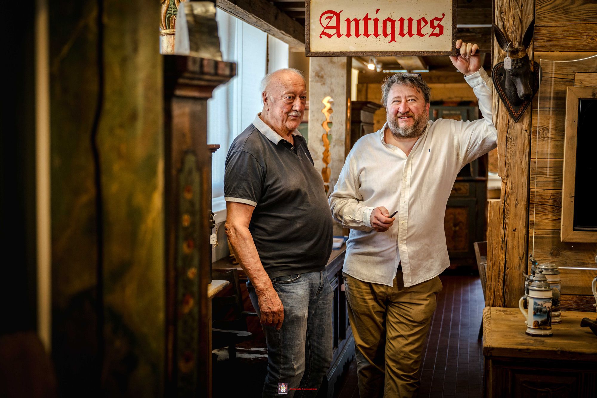 In un corridoio dell'esposizione, Leopoldo e Luca posano sotto un'insegna con la scritta Antiques