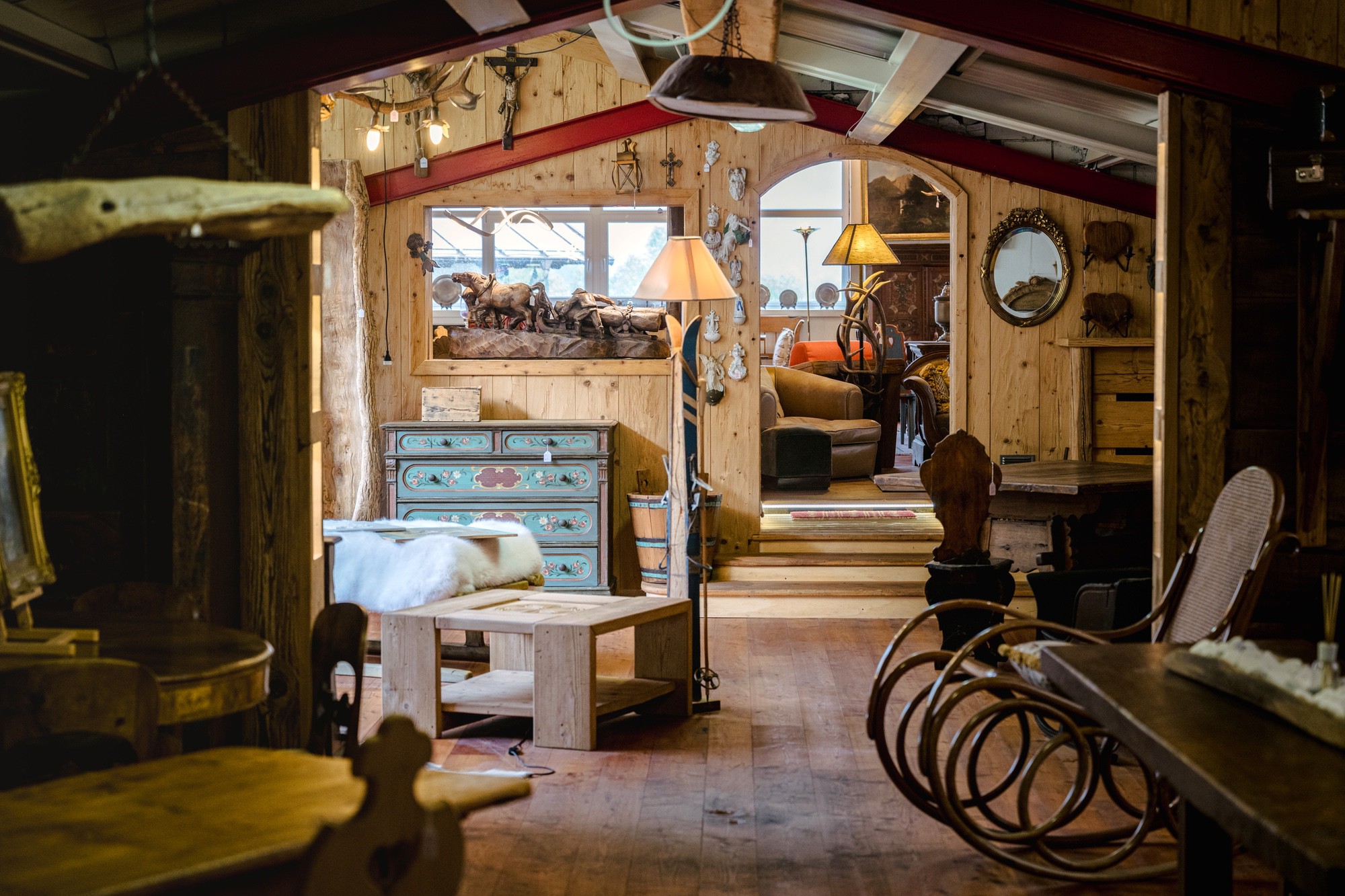 Complementi d’arredo in mostra Scultura in legno di cavalli al traino, lampade con paralume e specchio ovale dorato su pareti rivestite in legno