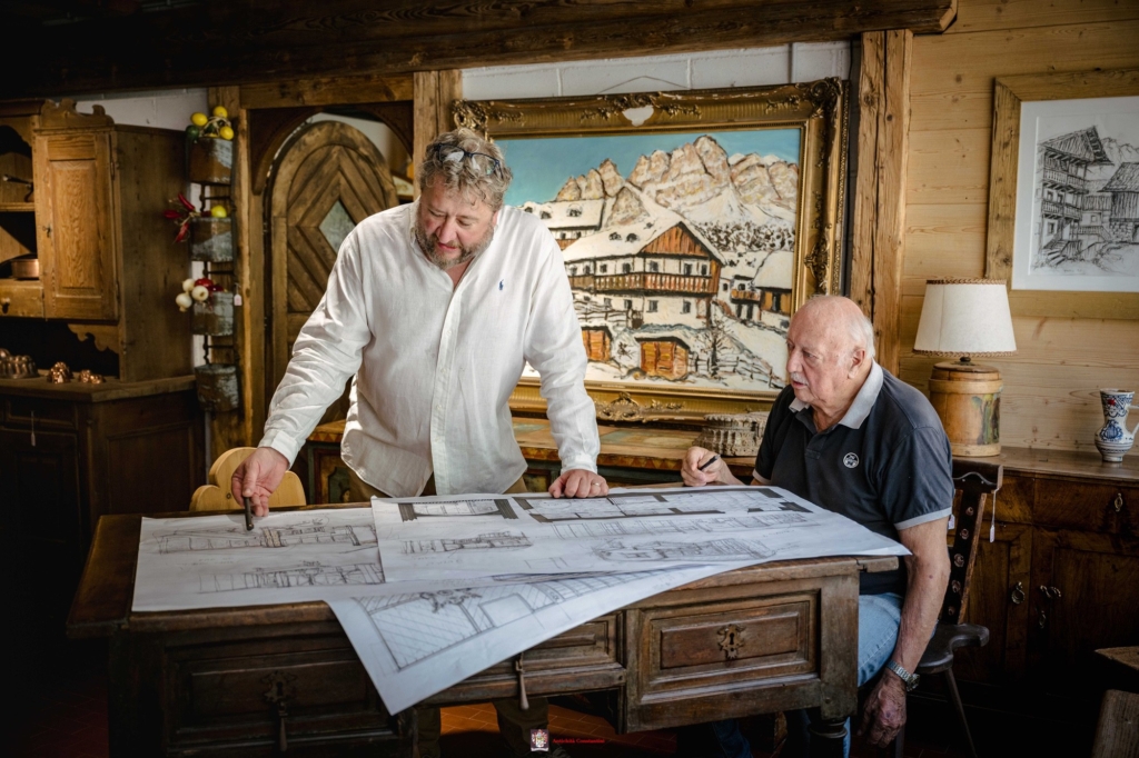 Schizzi di arredo sul tavolo, con Leopoldo e Luca Constantini davanti al dipinto di un paesaggio innevato di montagna