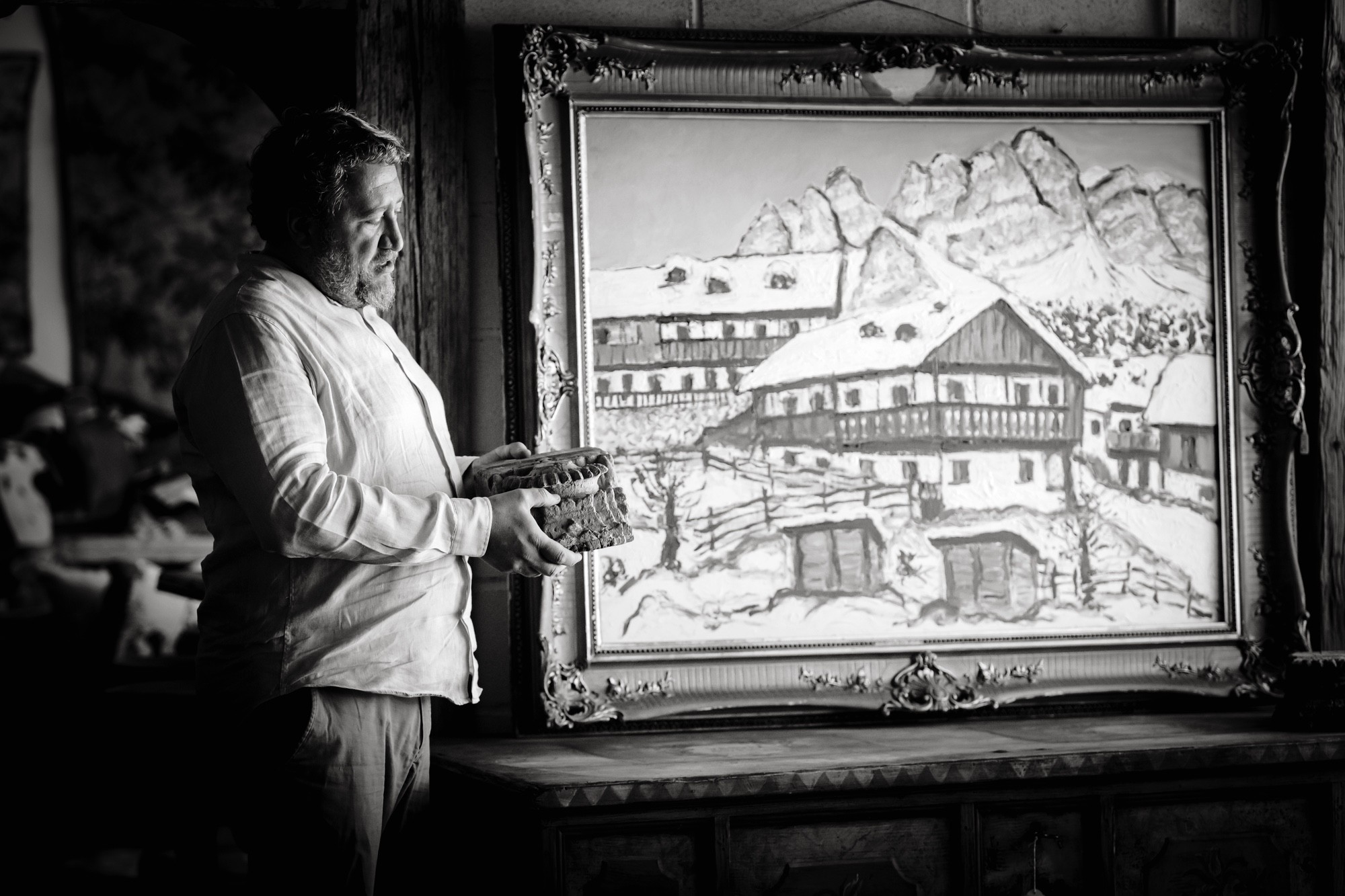 Luca accanto a un dipinto di montagna Ritratto monocromo di Luca che osserva un pezzo di legno intagliato, vicino a un quadro con un villaggio sotto la neve