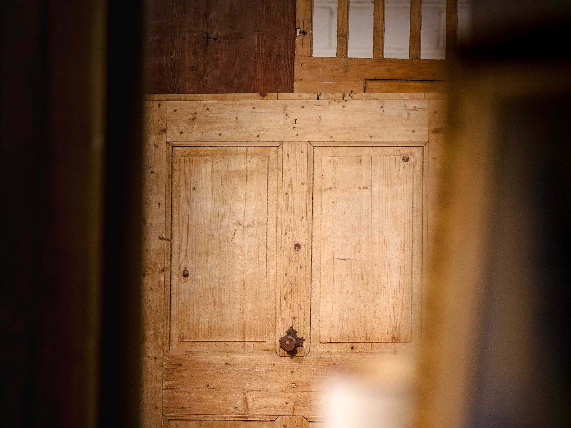 Porta in legno chiaro a due pannelli con pomolo in ferro, vista attraverso un'apertura sfocata