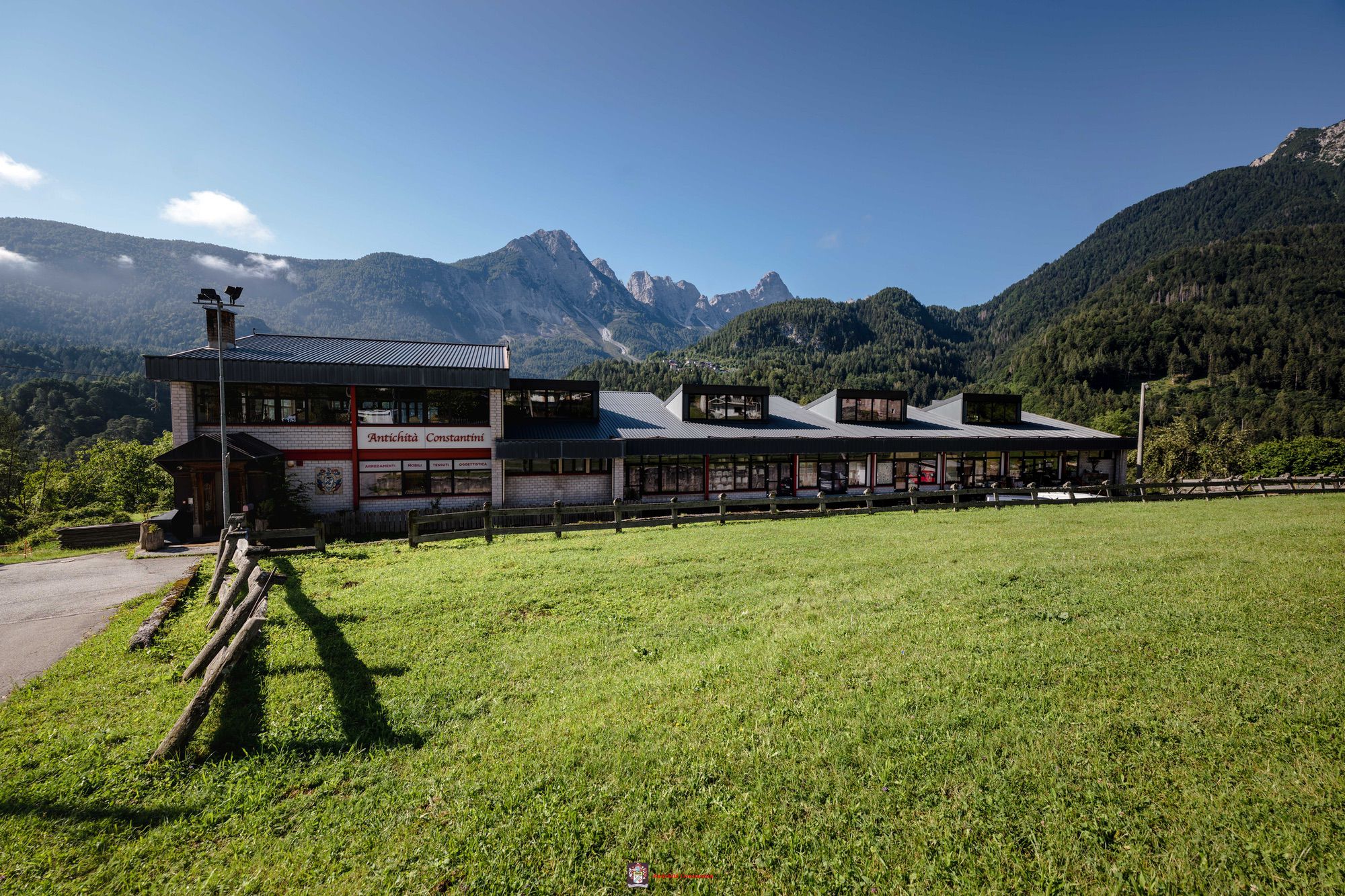 L'edificio di Antichità Constantini con l'insegna rossa, un prato recintato davanti e le montagne sullo sfondo