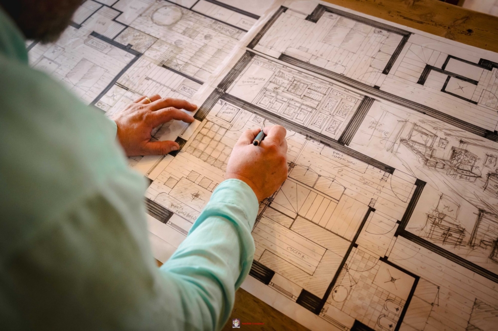 Progetto d’arredo disegnato a mano Luca che completa a matita la pianta di un'abitazione, con arredi, pavimenti e annotazioni tracciati a mano