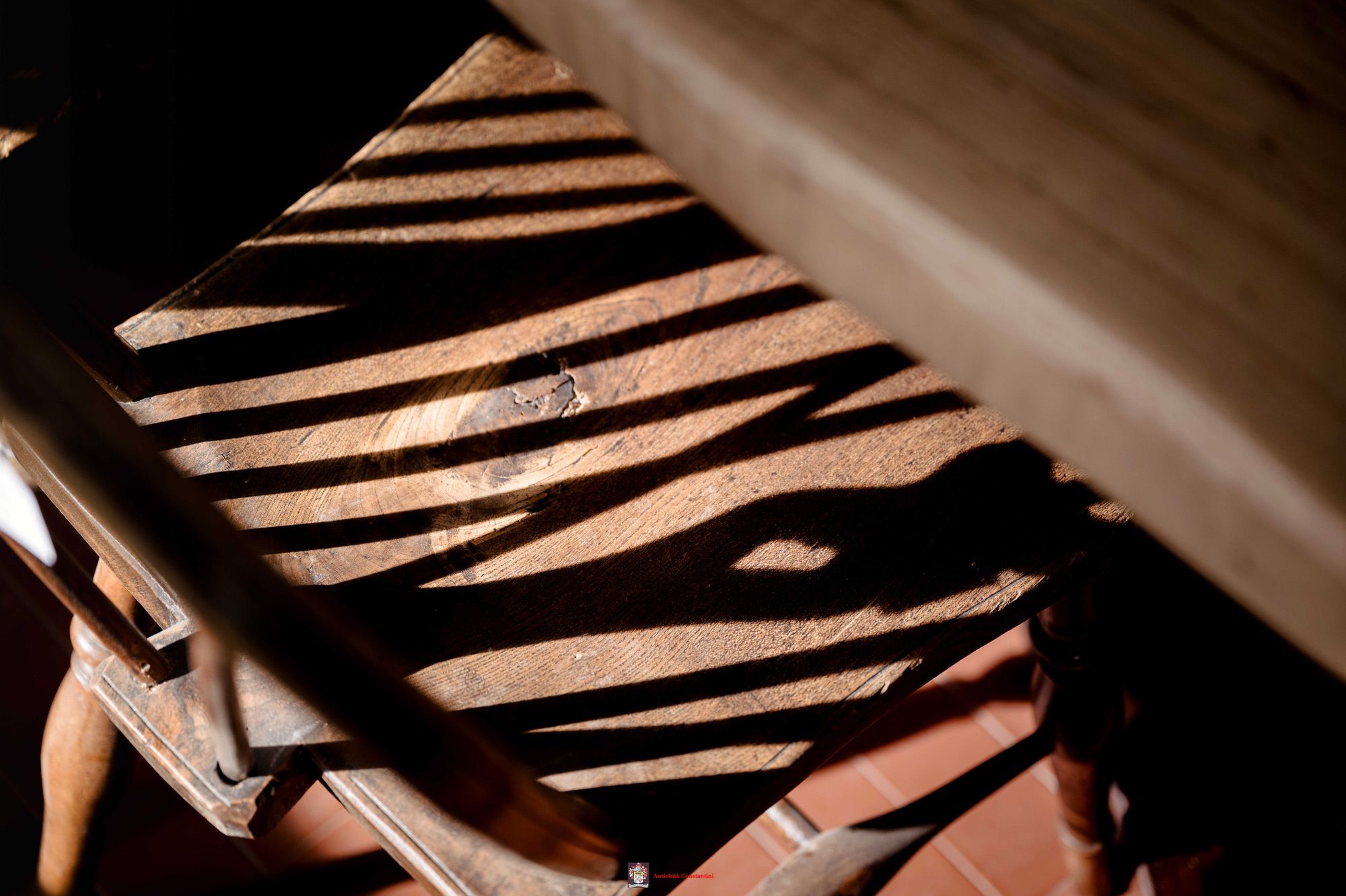 Luce radente che disegna strisce d'ombra sulla seduta consumata di una sedia in legno tornito